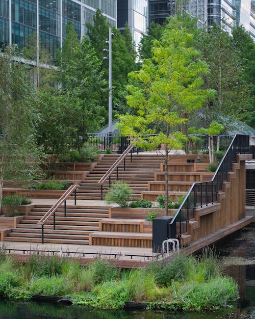 A multi-level outdoor garden area featuring wide wooden steps with integrated seating and black metal railings, surrounded by lush green trees and shrubs. The garden is situated near modern glass buil